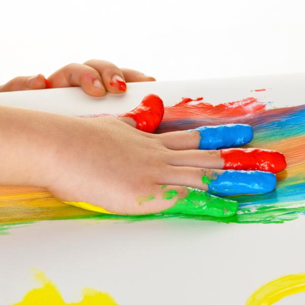Eine Kinderhand malt mit Fingerfarben einen Regebogen auf ein Blatt.